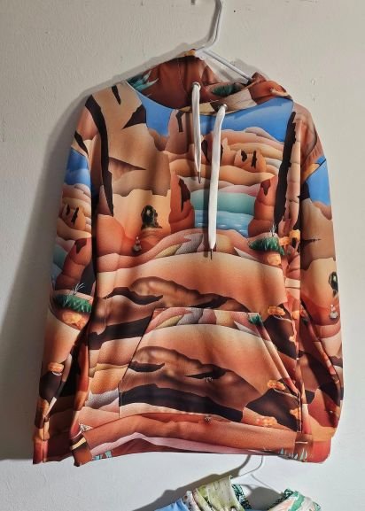 Southwest canyon landscape hoodie featuring Therese Tice’s original artwork, with layered desert rock formations, turquoise water, and warm earth tones printed on a pullover sweatshirt.