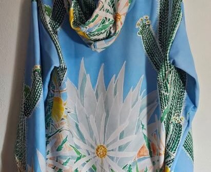Hand-painted hoodie by Therese Tice featuring desert cactus and white floral artwork on a light blue fabric.